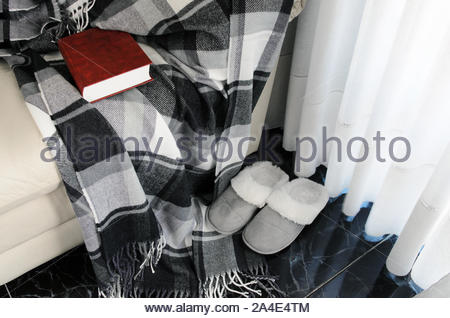 Woolen warm blanket and red book on white leather armchair, cozy .