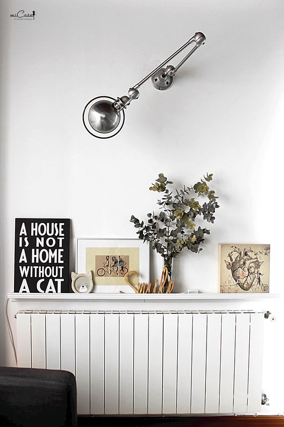 a white radiator with a matching white shelf and cool decor on it, with a wall lamp to make the radiator look cohesive