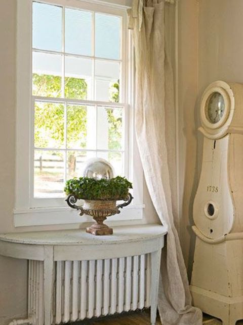 an antique table with a distressed white finish sits on the radiator turning it into a comfortable shelf that may be used for decor