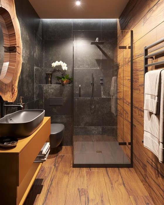a bold bathroom clad with wood look and black stone tiles, a floating vanity with a black sink, a mirror in a living edge frame and lights