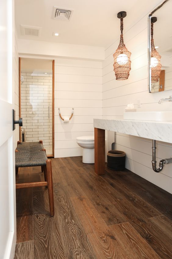 a catchy bathroom with shiplap walls and a rich-stained wood tile floor, a shower space, a long vanity and a unique lamp