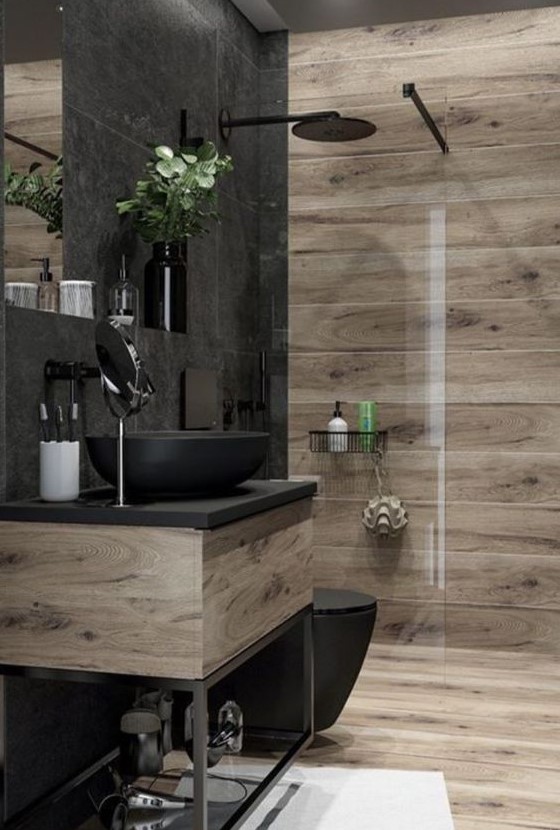 a contemporary bathroom clad with wood look and stone tiles, with a wooden and metal vanity, black appliances and black fixtures is stylish