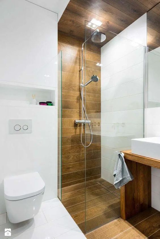 a contemporary bathroom with white and wood-inspired tiles, a vanity, a shower and a mirror plus built-in lights