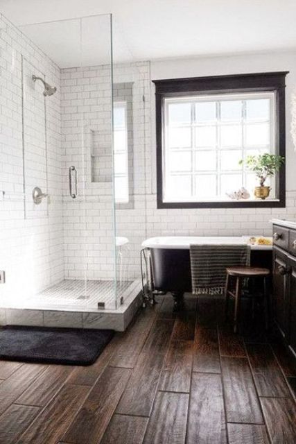 a farmhouse bathroom with white subway tiles, a dark wood tile floor, a black clawfoot tub and a black vanity is cozy and cool