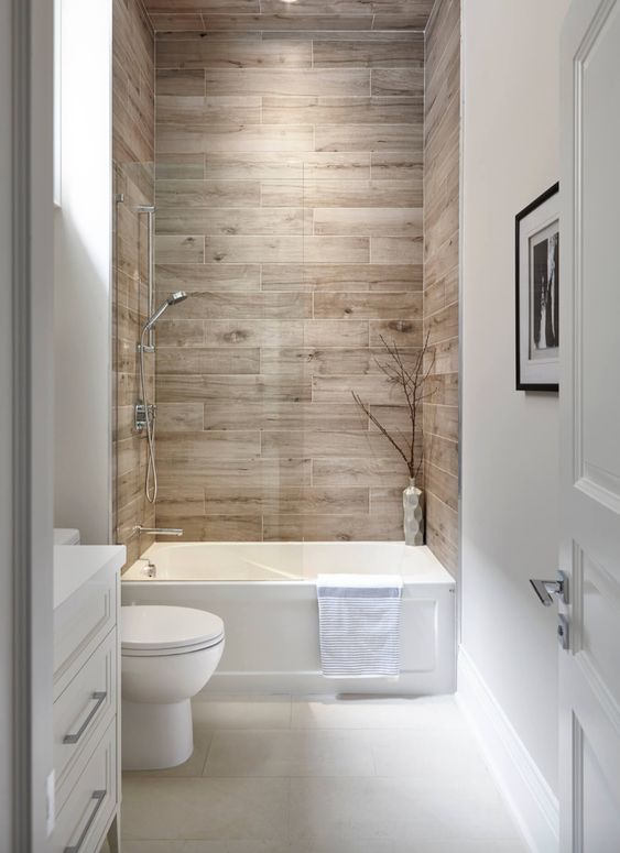 a neutral bathroom with wood tiles, a small tub, a toilet and a built-in vanity is a cool and laconic space