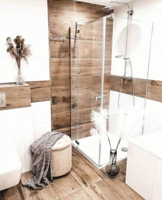 a neutral boho bathroom with wood and large scale white tiles, a small shower, a white vanity and a toilet plus a pouf