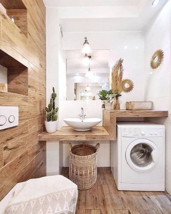 a small boho bathroom clad with wood tiles, with a wooden vanity that includes a washing machine, some potted plants