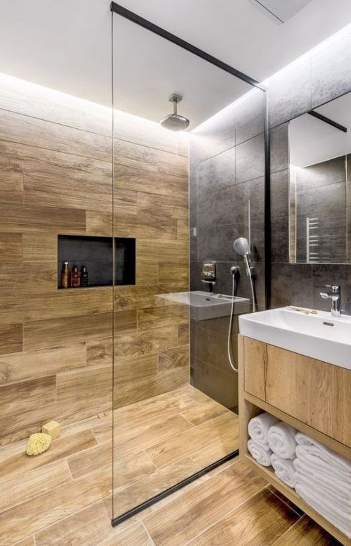a stylish contemporary bathroom clad with black stone and wood look tiles, a niche, a light stained vanity and white appliances