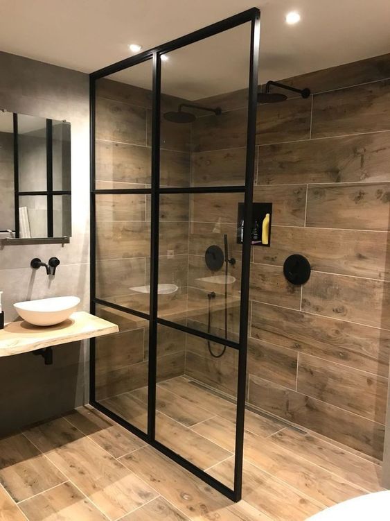 a bold contemporary bathroom with wood look tiles, a wooden vanity and black framing for a dramatic touch