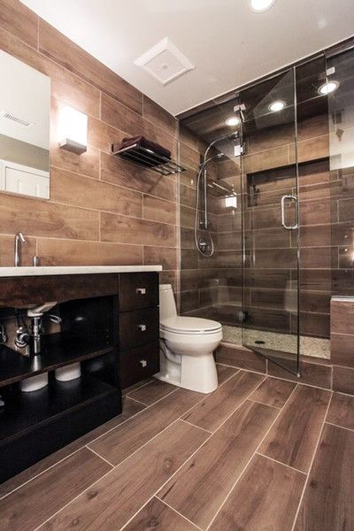 a modern rustic bathroom all clad with wood look tiles, with a dark vanity and shiny fixtures for a brighter look