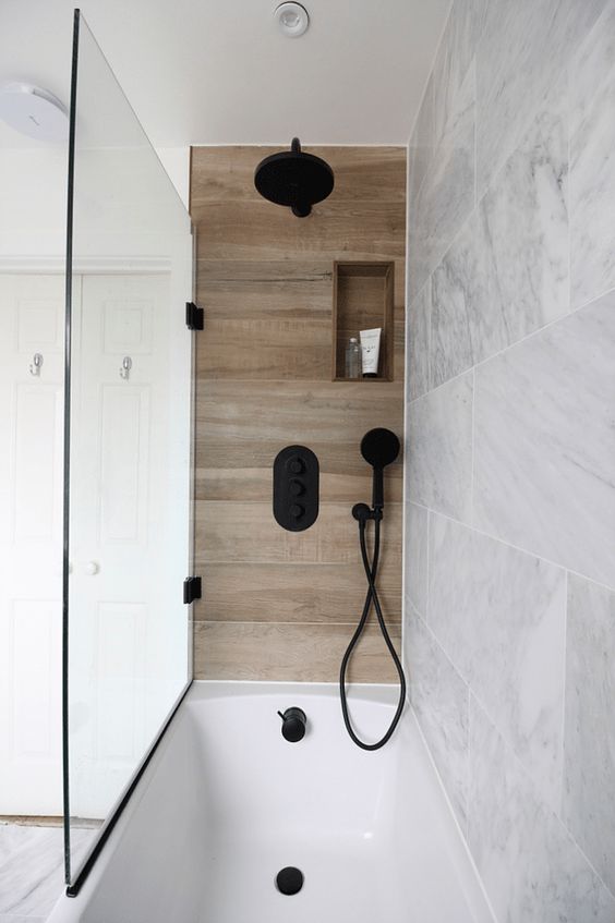 a neutral marble bathroom and a small wood look tile accent in the bathing space plus black fixtures