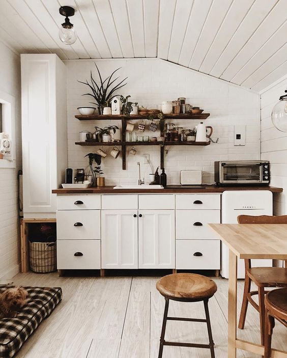 a white Scandi kitchen with sleek cabinets, a blonde wood table and matching chairs, dark-stained butcherblock countertops