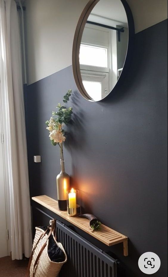 a black radiator with a small stained fluted shelf, with blooms, a candle and a round mirror over it