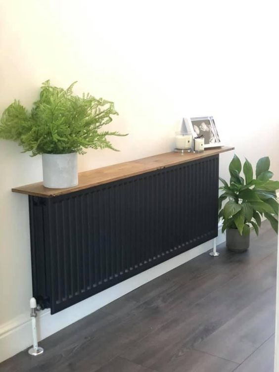 a black radiator covered with a stained shelf with potted plants, candles and some decor is a very natural console table