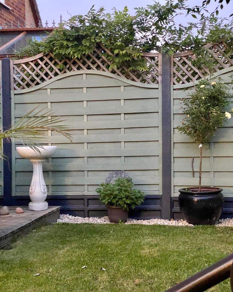 green wooden fence with black base, black potted plant, white stone water feature 