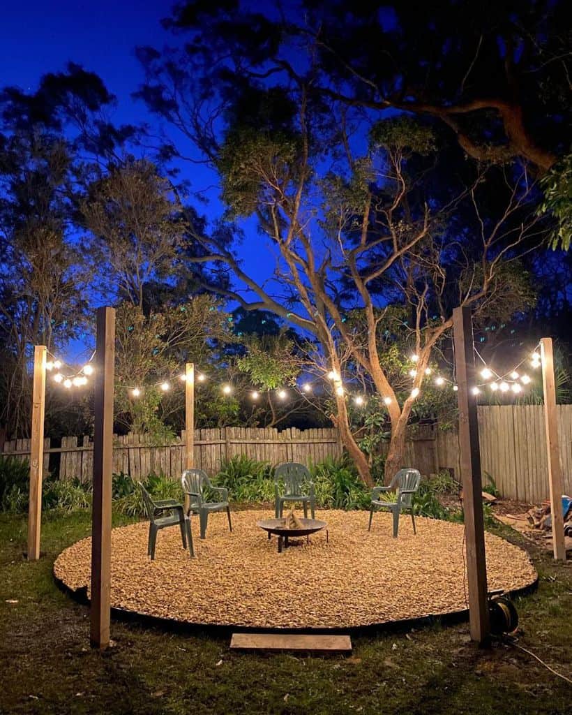 Gravel outdoor area with fire pit, green plastic chairs and fairy lights 