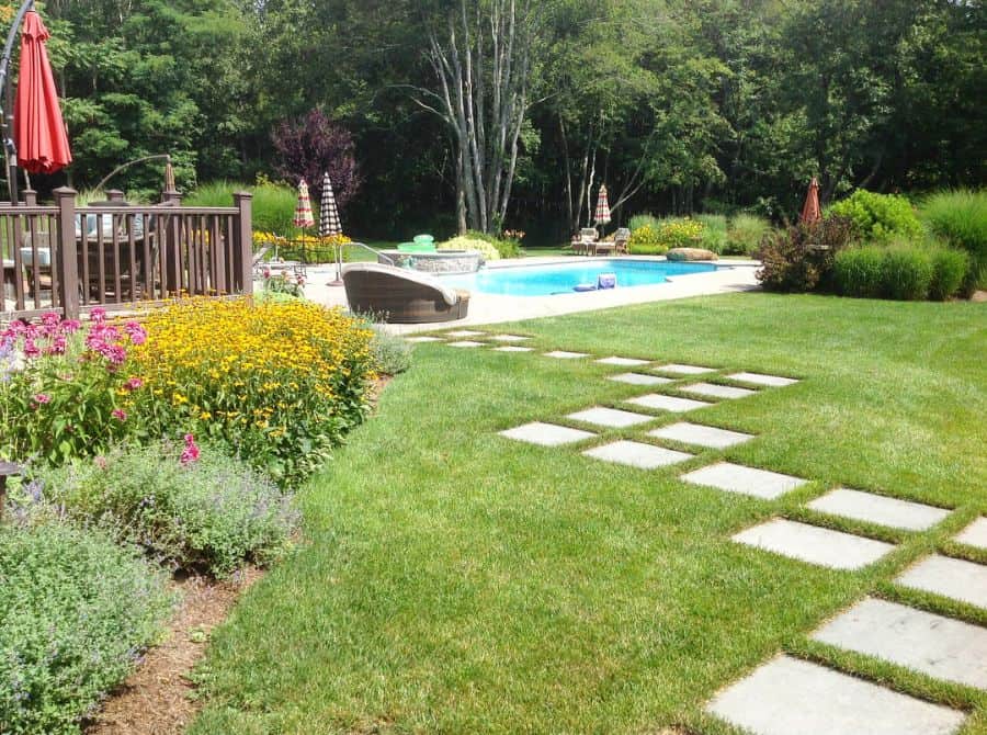 Large paved path in the backyard through grass to the wooden deck of the pool terrace 